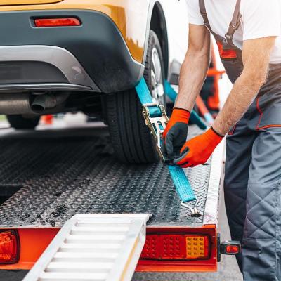 Close up of older man securing a yellow car to a flatbed tow truck with ratchet straps.