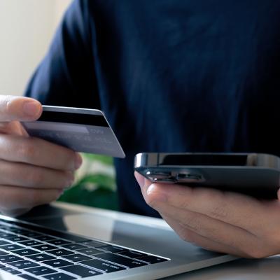 A person holding a credit card, making a purchase payment using a laptop and a phone.