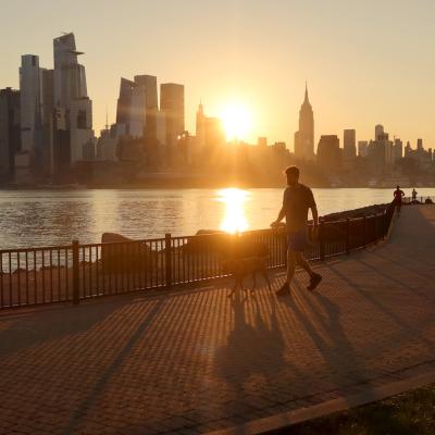 A person walks their dog in Hoboken, New Jersey, along the Hudson River, as the sun rises behind the skyline of Manhattan during a heatwave in September 2023.