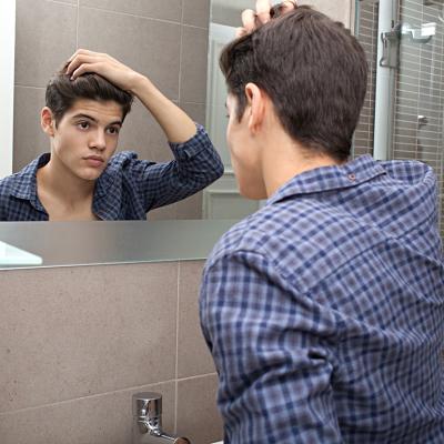 Young teenage man looking at himself in a bathroom mirror at home doing his hair.