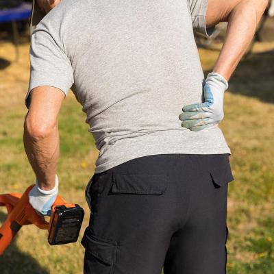 View from behind of person pushing lawn appliance while holding arm to back in pain.