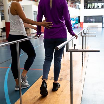 A female physical therapists assist a patient in a walking practice.