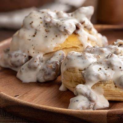 Closeup of biscuits and creamy sausage gravy on a wooden plate.