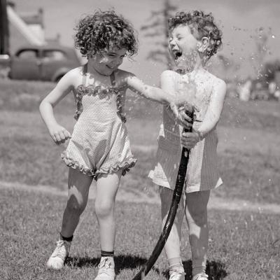 Children in the 1950s splashing water from a garden hose during the summertime.