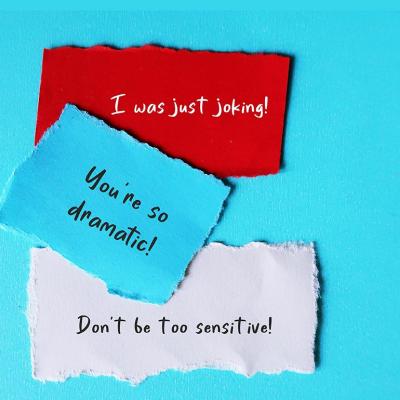 Notes saying "I was just joking," "don't be so dramatic," and "don't be too sensitive!" written on paper and stuck to blue background. 