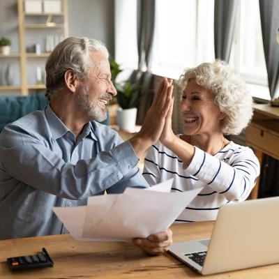 A baby boomer couple giving each other high five while doing finances.