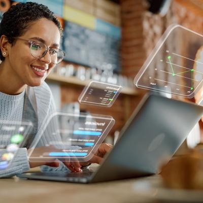 A female business owner using a laptop and illustrated with different holographic icons representing apps.