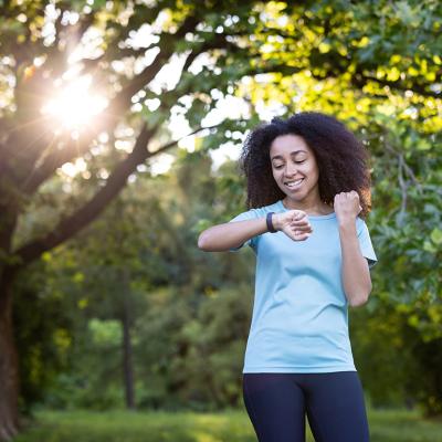 A young lady exercising outdoors is looking at her fitness tracker watch.