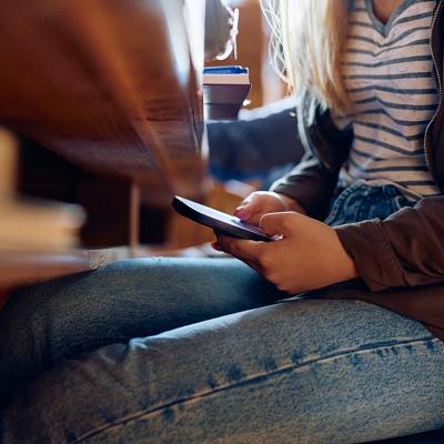 Young student using cell phone under a desk during class.