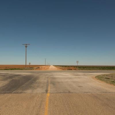 A rural intersection in Texas with a stop sign and a blue sky in the background.