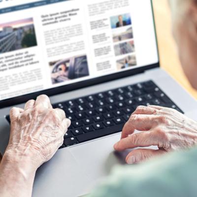 View of older person from behind looking at news website on laptop computer.