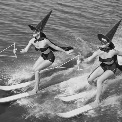 Two women dressed in black swimsuits and witch hats on jet skis