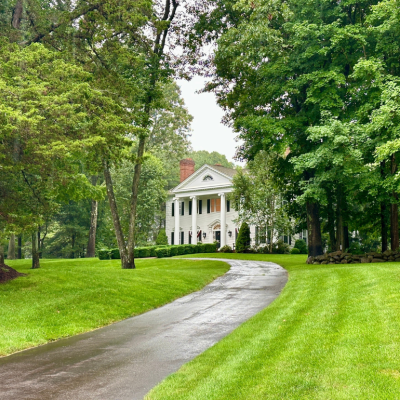 A colonial-style white house at the end of a long driveway in an affluent neighborhood in Madison, Connecticut