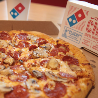 A pepperoni and mushroom pizza from Domino's, with a Domino's box and drink cup in the background