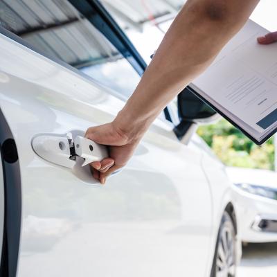 Person inspecting a car while filling out a car insurance form.