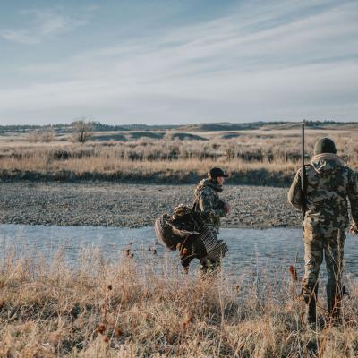 Two people out hunting in a vast field.