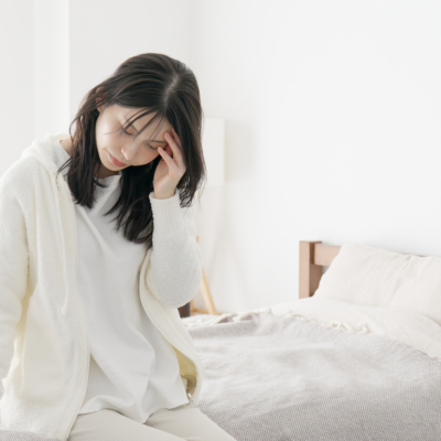 Unwell woman sitting on the edge of a bed with a hand on her forehead