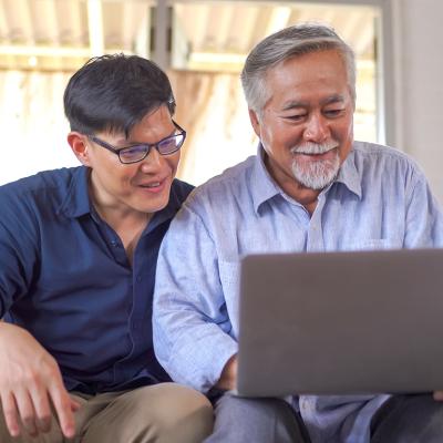 A senior father and his young son looking at information using a laptop at home.