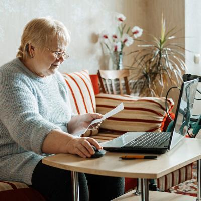 An older woman with disability looking up insurance information online using a laptop.