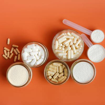 Flatlay of different types of vitamins, supplements and protein powder displayed with an orange background.