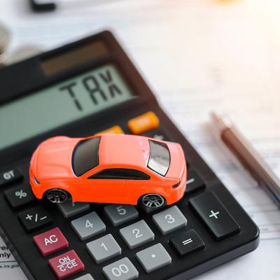 A miniature car figure on top of documents and a calculator indicating 'tax'.