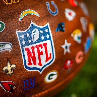 A focus shot on an NFL game ball featuring all logos of NFL teams.