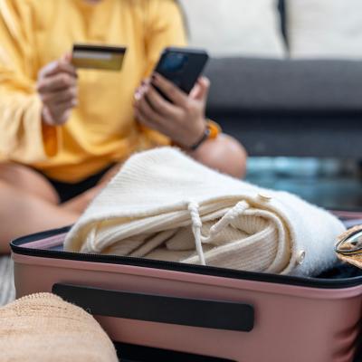 A woman planning a trip using credit card and phone while preparing a suitcase.