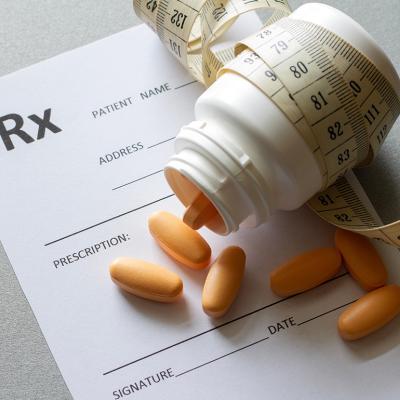 Bottle of pills wrapped with a tape measure on top of a prescription.