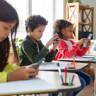 Diverse group of schoolkids using smartphones in classroom.