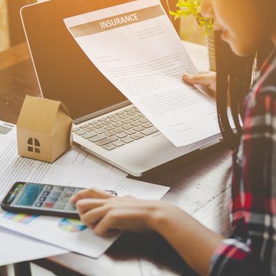 A young woman looking up information on home contracts and insurance using a phone and a laptop.