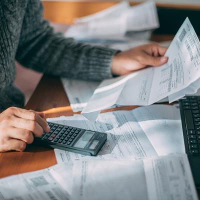 Person holding loan and utility bills while using a calculator.