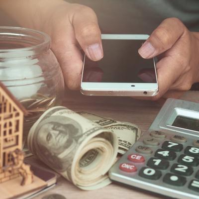 Person holding a phone with money, a figure of a house and savings around to represent passive income.