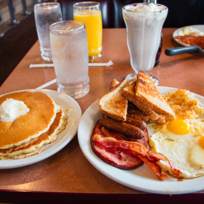 Plates of pancakes and fried eggs, bacon, sausages and toast on a diner table