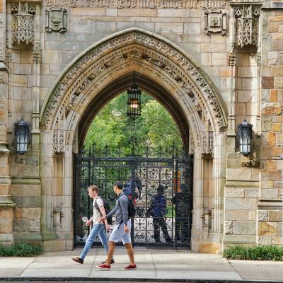 Students walk past a decorative stone archway at the entrance to Yale University in New Haven, Connecticut.