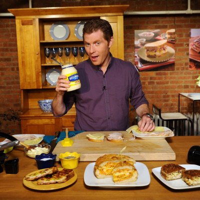 Chef Bobby Flay holding up a jar of mayonnaise in front of a countertop with plates of food, circa 2011.