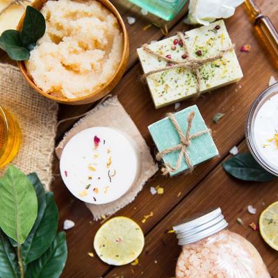 Top down view of lotions, soaps, and beauty products with flowers and plants incorporated on a wood table.