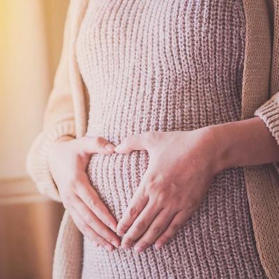 Photo of woman wearing a sweater dress holding hands over belly in a heart shape. 