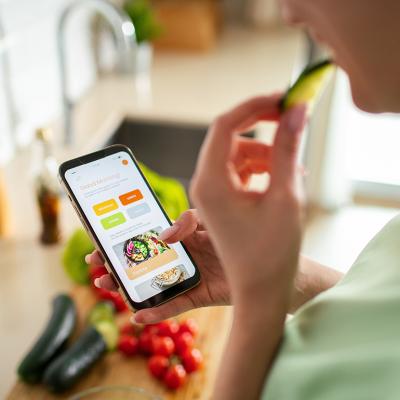 A woman is looking up meal plans on her phone while preparing food.