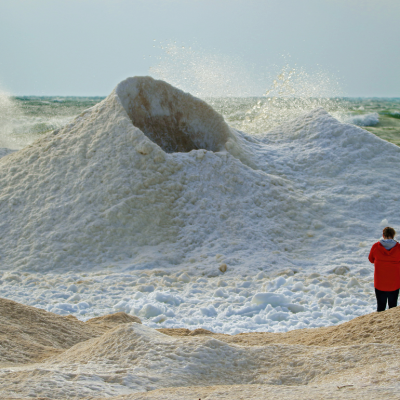 Person standing next to an ice volcano on the shores of Lake Michigan