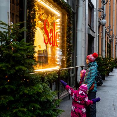 A mother and son looking at a boutique's window with a huge sale sign during Christmas shopping season.