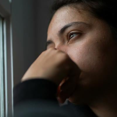 A pensive young woman sitting by a window looking outside.