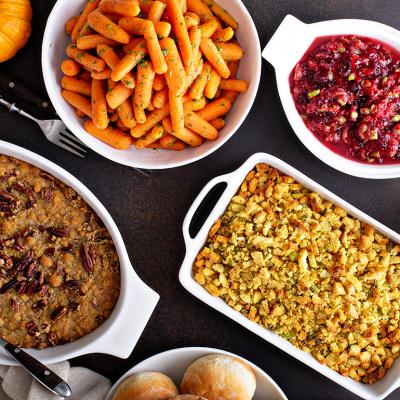 Thanksgiving side dishes such as mashed sweet potatoes, baked vegetables and mac and cheese are laid out on a table.