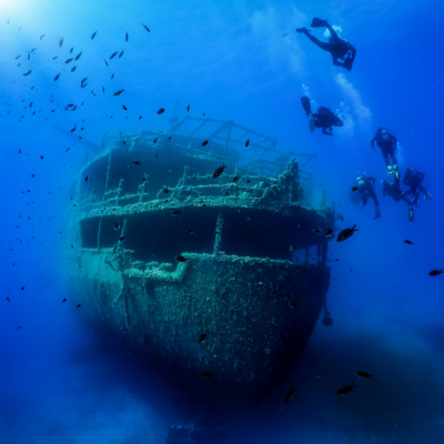 A group of divers explore a sunken shipwreck in the blue, Mediterranean sea at Naxos island, Greece