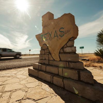 A car speeds along past a border sign for the state of Texas.