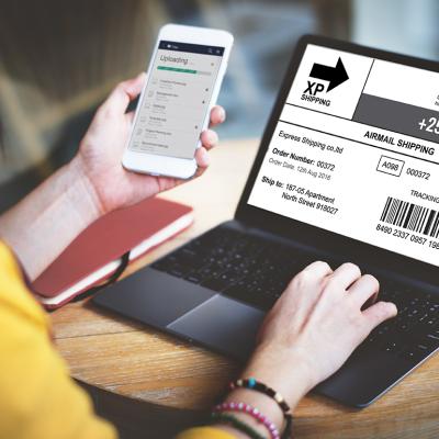 A woman using a laptop and phone to check a parcel's tracking number and progress.