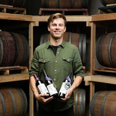 Ben Justman posing with wine bottles in a cellar.