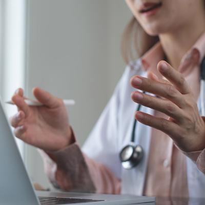 Generic medical professional (without face visible) gesturing in front of laptop computer.