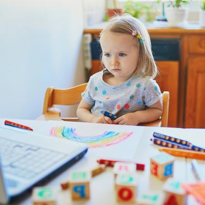 A toddler girl focused on watching in front of a laptop.