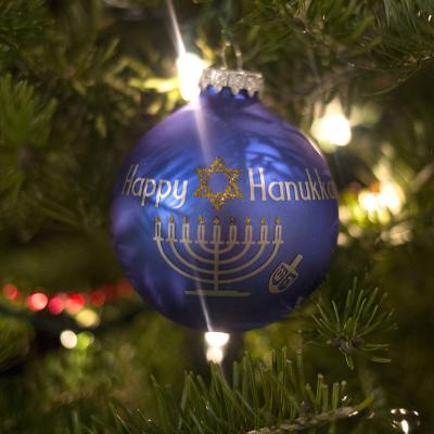 A blue "Happy Hanukkah" ornament hangs on a Christmas tree.