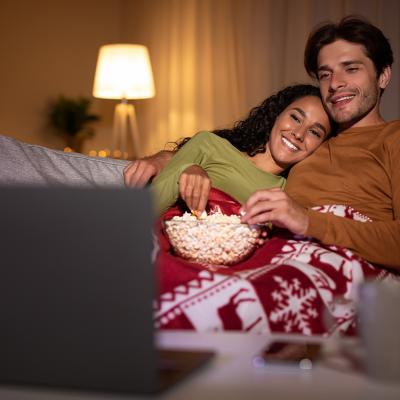 A couple eating popcorn enjoying a movie from a laptop during the holidays.